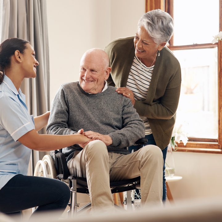 Cropped shot of an attractive young female nurse standing next to an elderly male tenant in a wheelchair and his wife at an old age home